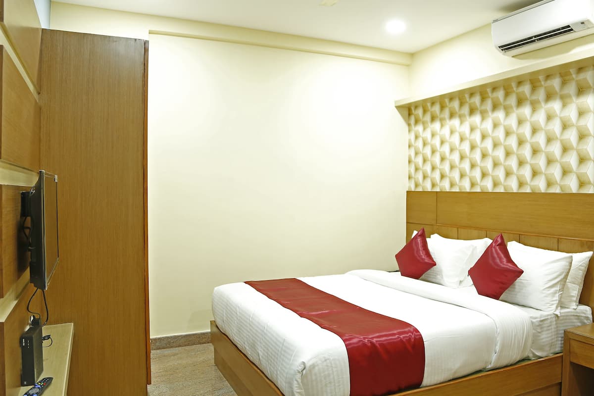 A hotel room with a wooden bed, white bedding, red pillows, a wooden nightstand, and a wall-mounted air conditioner.