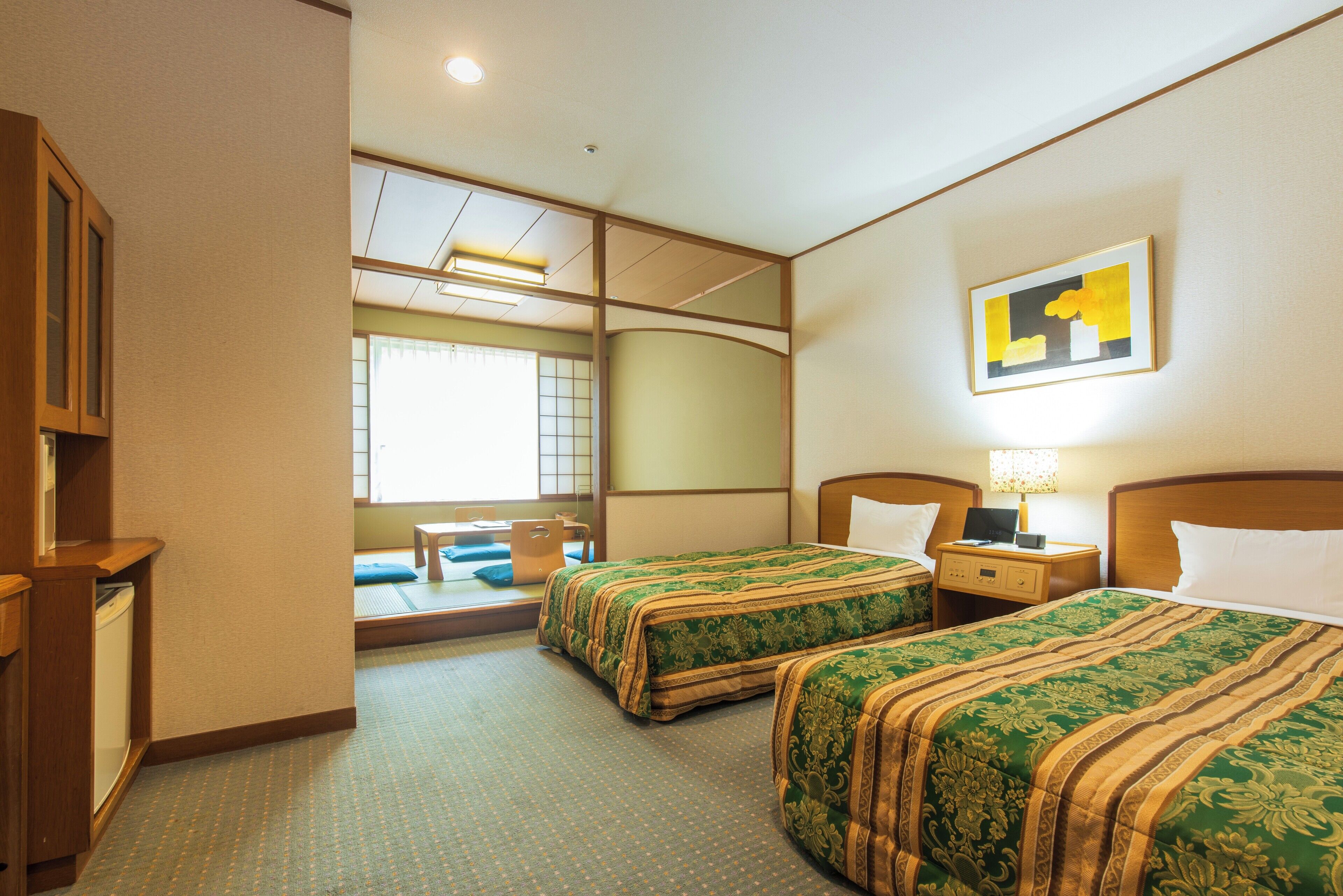 A hotel room with two beds, a desk, a chair, a small table, and a window with a view of a building.