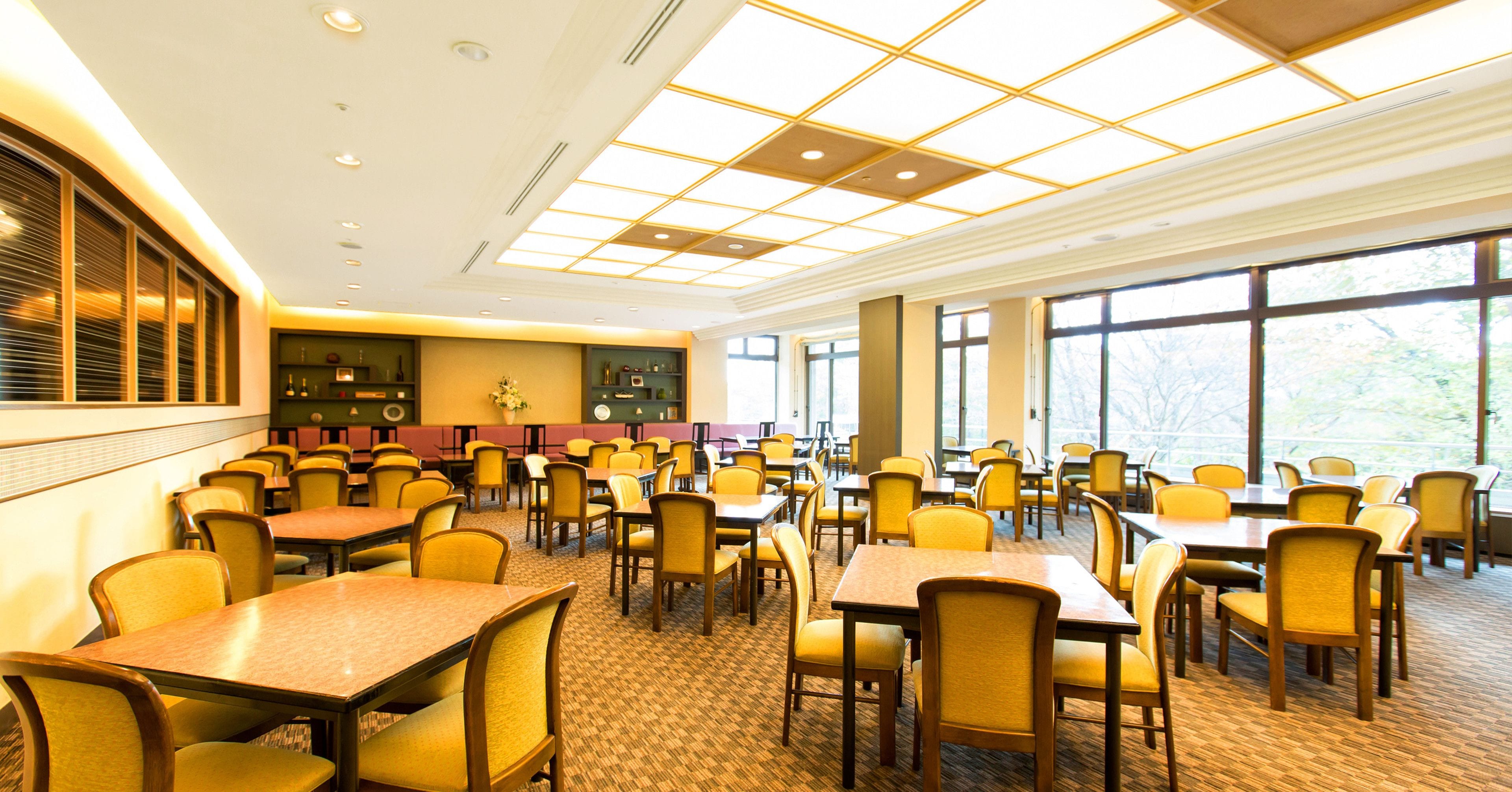 A spacious dining area with multiple tables and chairs, large windows, and a modern ceiling design.