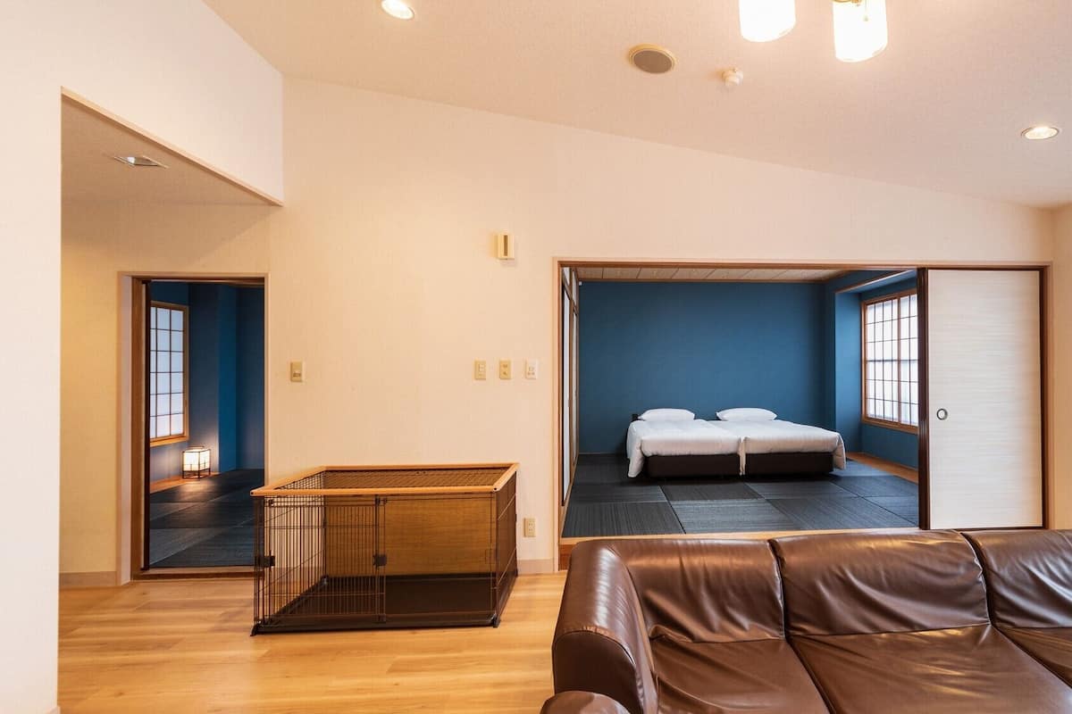Une chambre d’hôtel moderne avec un plancher en bois, un canapé en cuir, un lit avec une literie blanche et une porte coulissante donnant accès à la salle de bain.