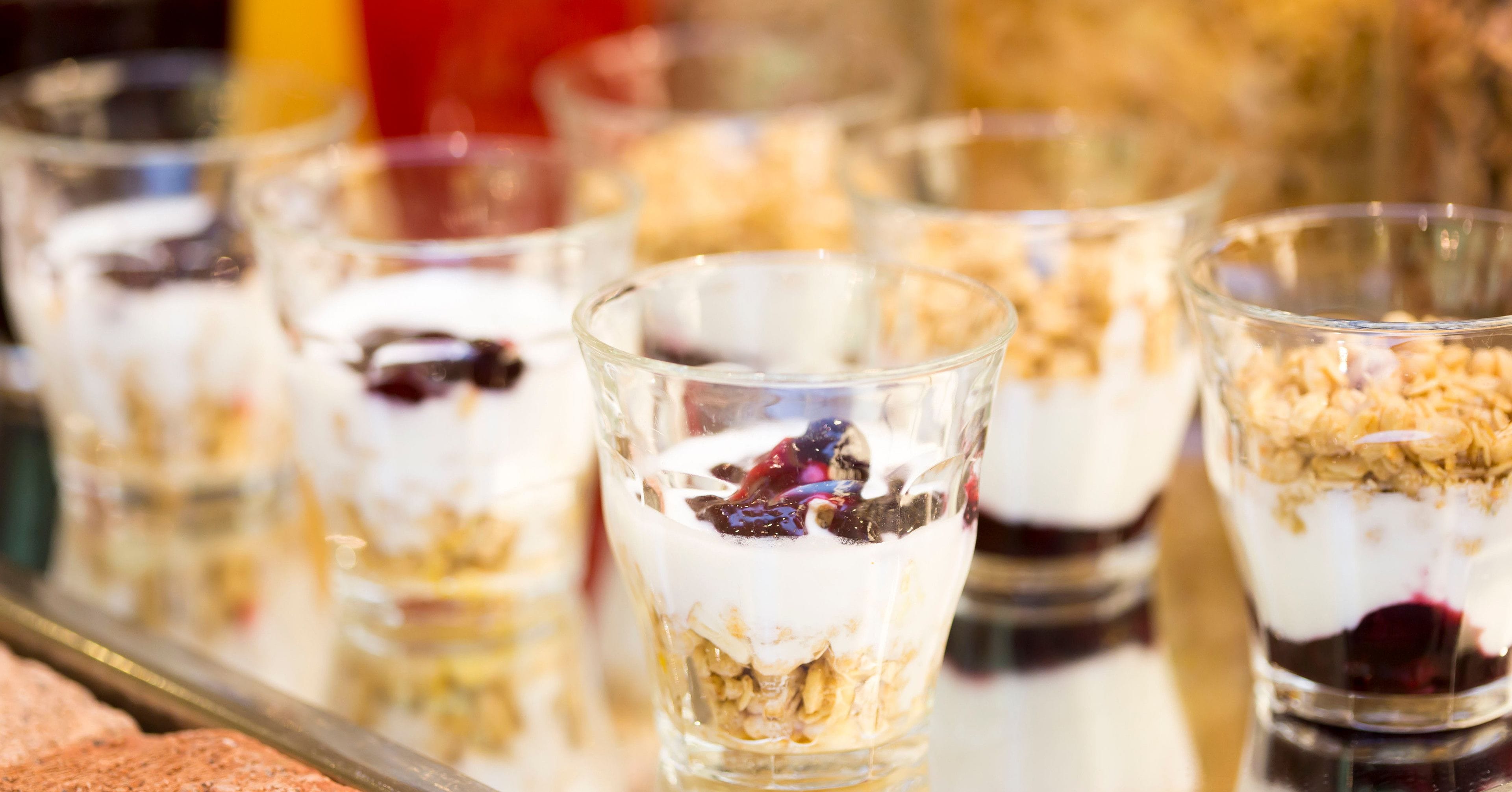 Una serie de vasos transparentes llenos de capas de alimentos, probablemente un postre o parfait, sobre una superficie reflectante.