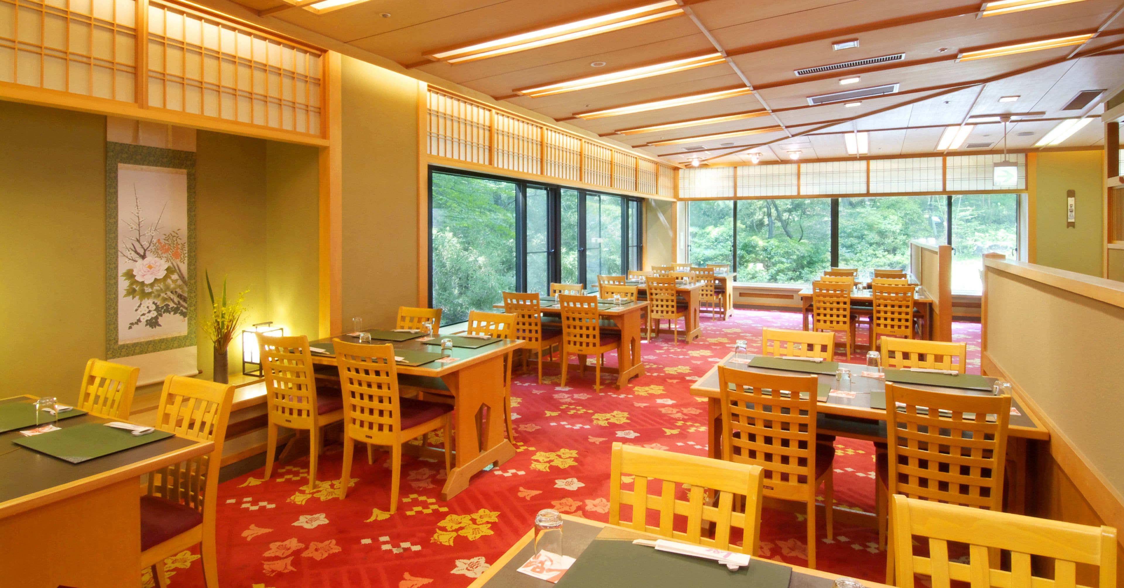 Une pièce de style japonais traditionnel, avec un sol recouvert de tatamis, des meubles en bois et de grandes fenêtres donnant sur un paysage verdoyant.