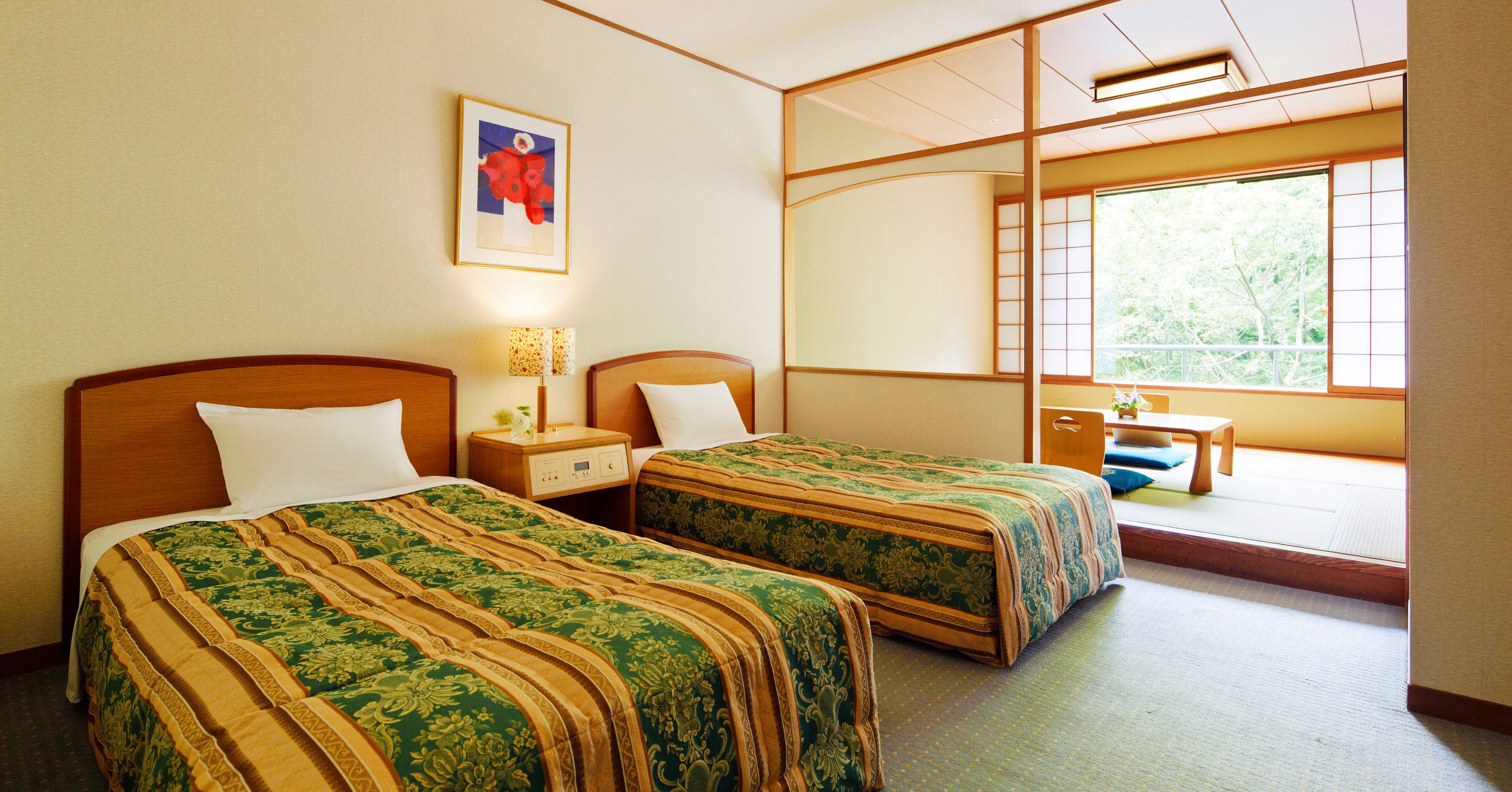 A hotel room with two beds, a nightstand, a bedside table, a window with a view of greenery, and a framed picture on the wall.