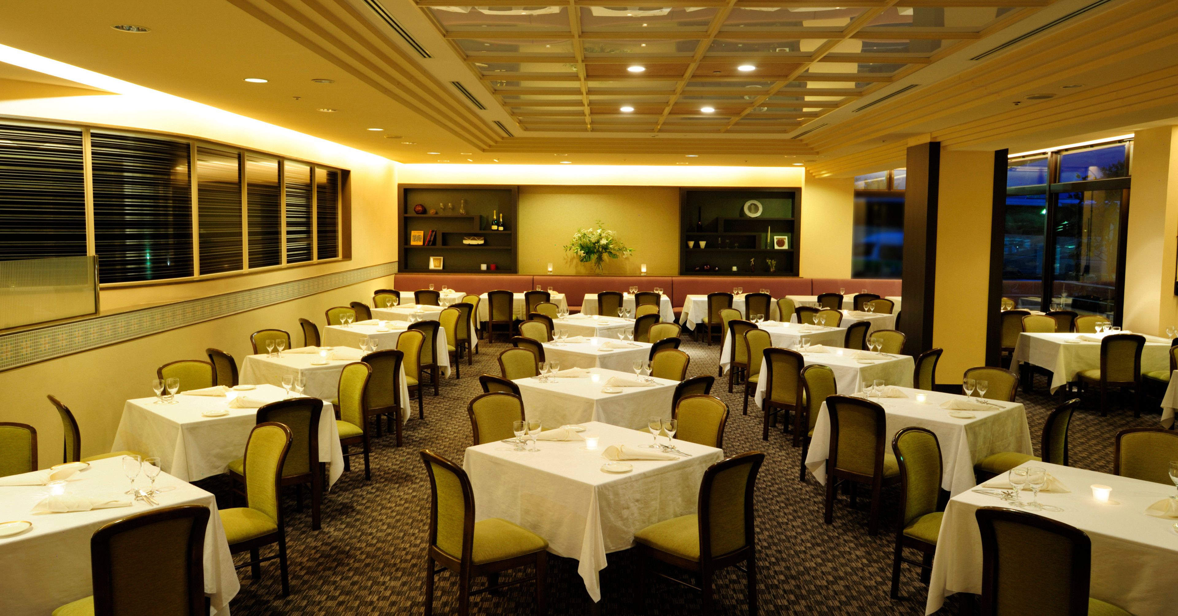 A banquet hall with multiple tables and chairs, arranged in rows, with a decorative wall and a window on one side.