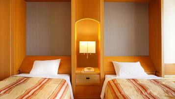 A hotel room with two single beds, a bedside table with a lamp, a phone, and a control panel.