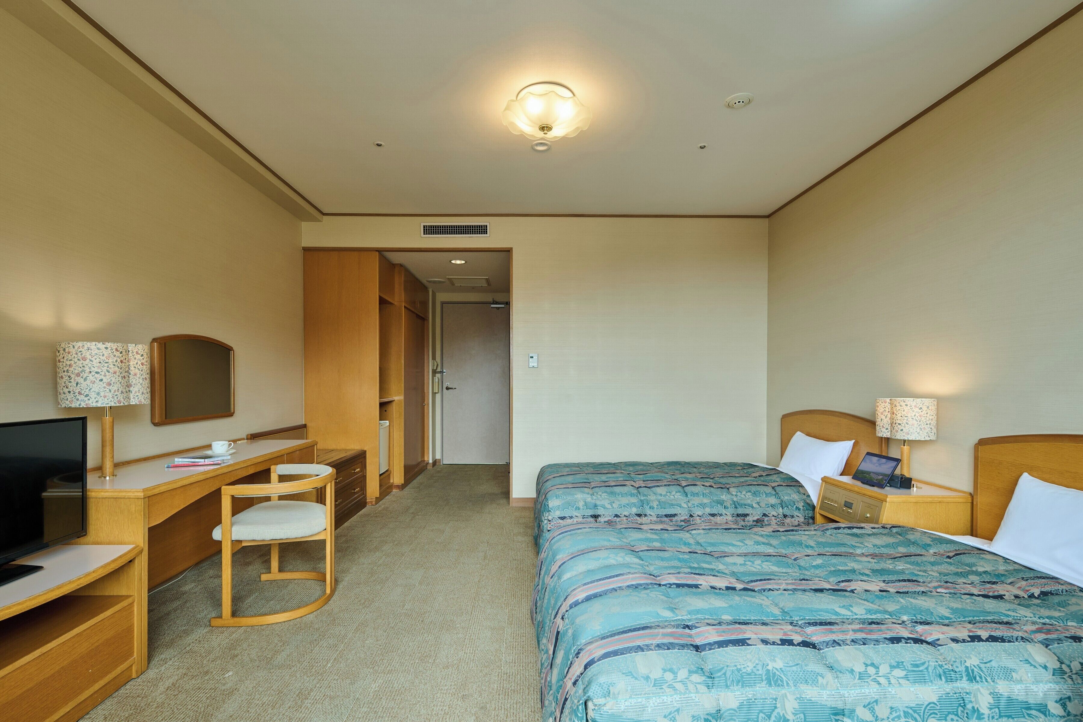 A hotel room with a bed, a desk with a chair, a television, and a lamp.