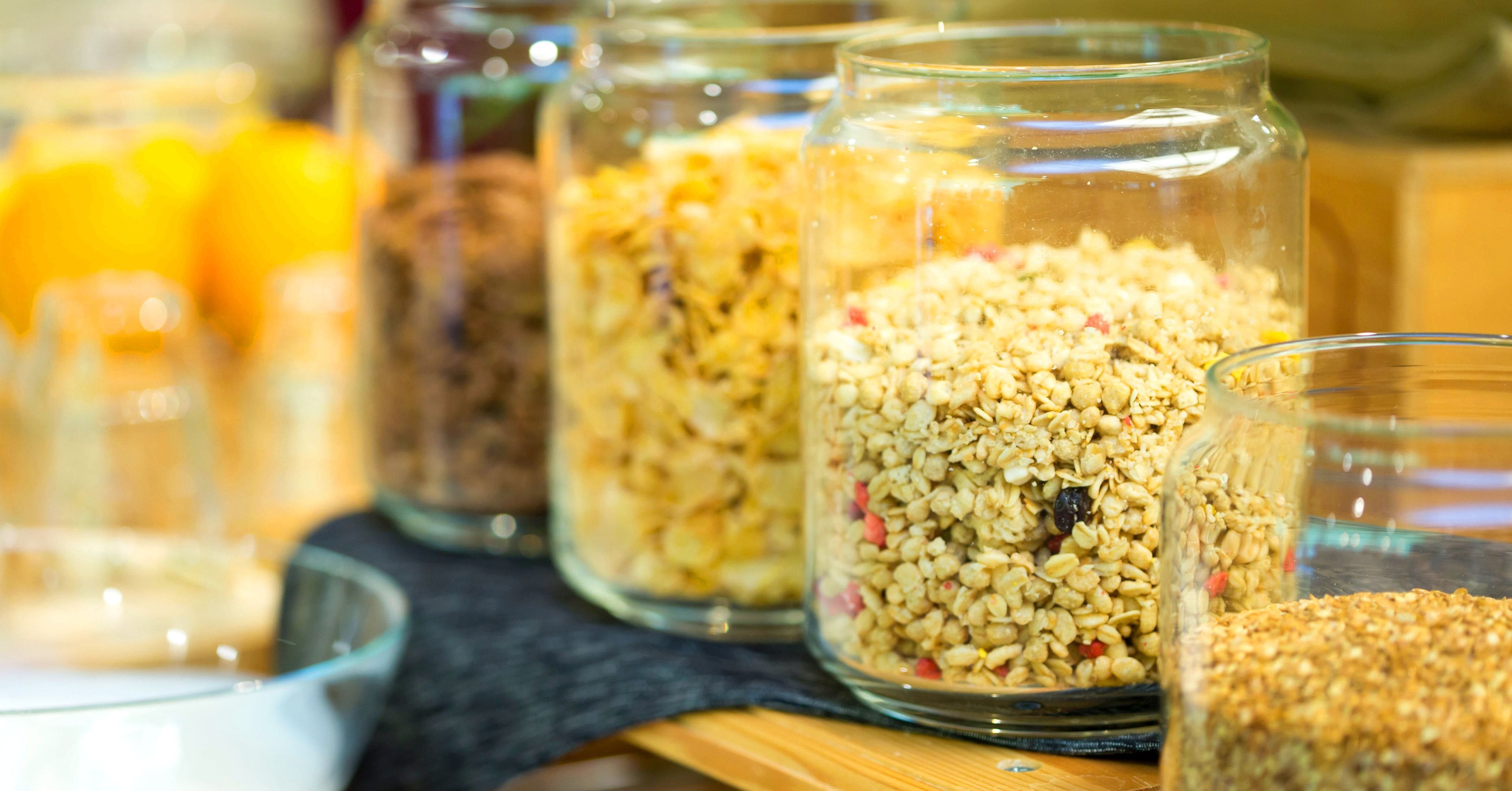 Tarros de vidrio llenos de diferentes cereales y semillas sobre un estante de madera.