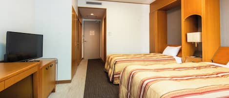 A hotel room with a TV on a desk, two beds with striped bedding, a carpeted floor, and wooden paneling.