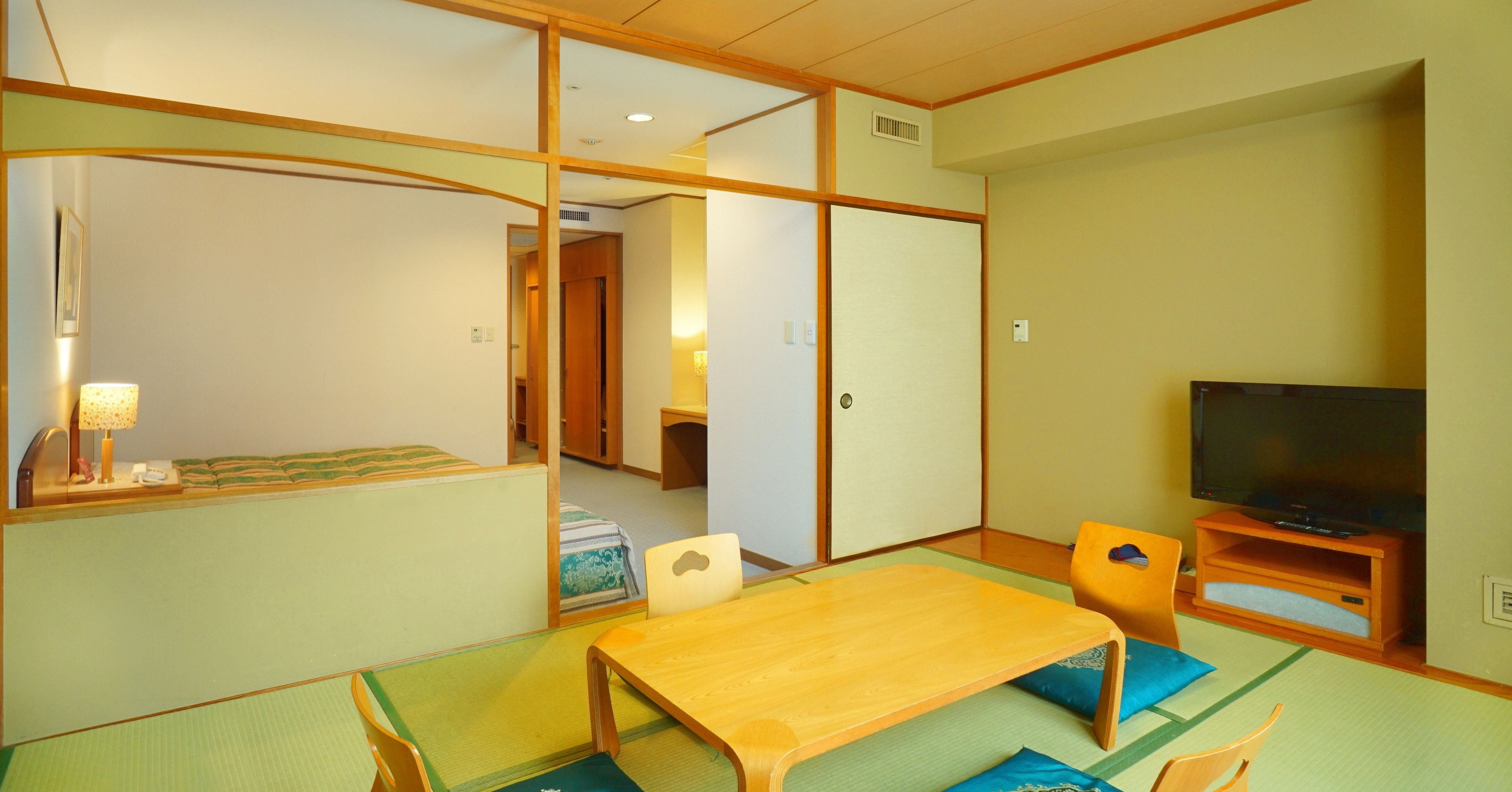A traditional Japanese room with tatami flooring, a low wooden table, a television on a wooden stand, and sliding doors.