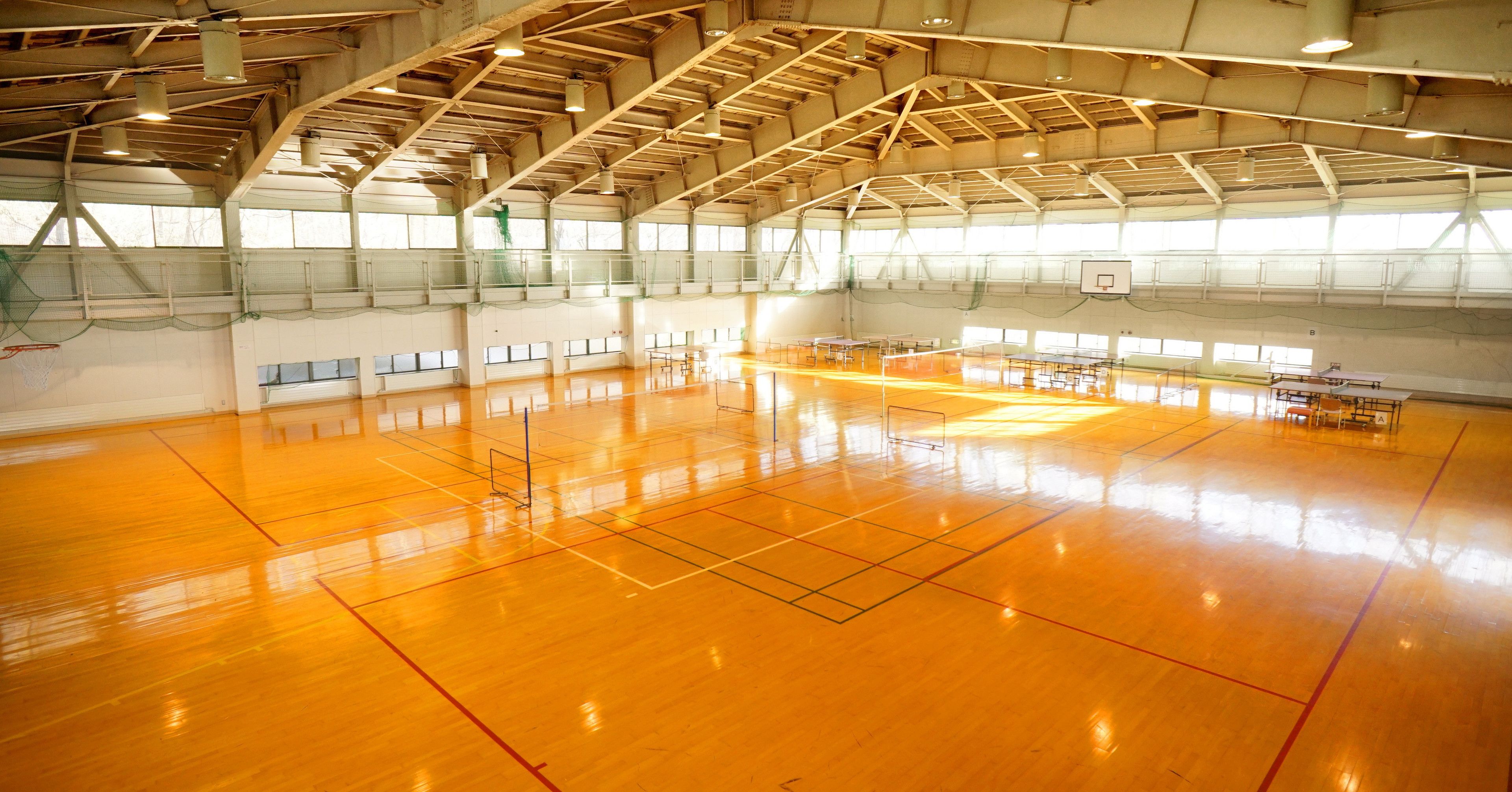 An indoor gymnasium with a high ceiling, basketball hoops, and a polished wooden floor.