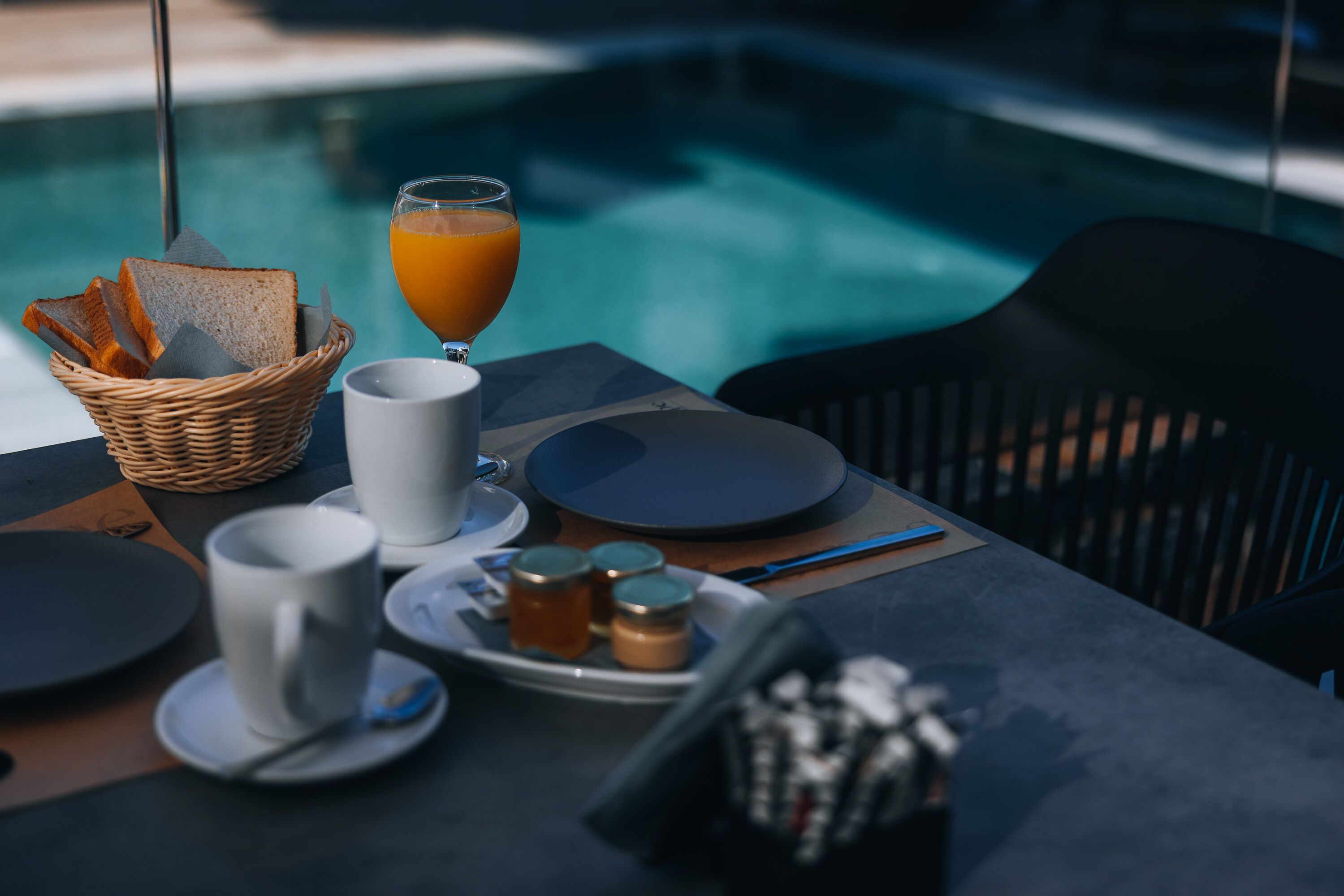 Un buffet de petit-déjeuner installé au bord de la piscine, avec des toasts, du jus de fruits, du café et diverses garnitures.