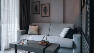 Uma sala de estar moderna com um sofá cinzento, duas folhas emolduradas na parede e uma mesa de centro com uma vela e uma pequena planta.