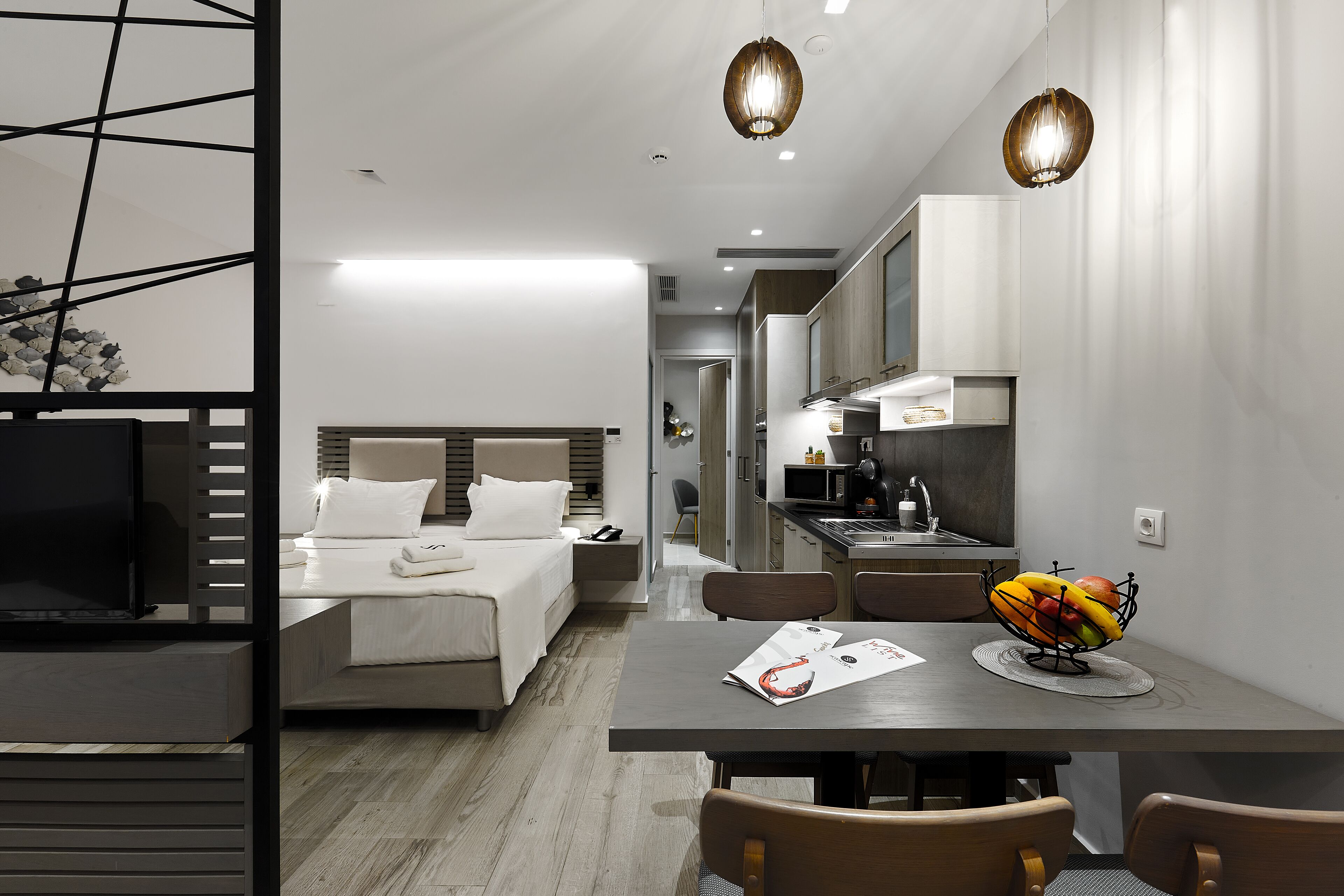 A modern hotel room with a bed, bedside table, and a dining area with a table and chairs.