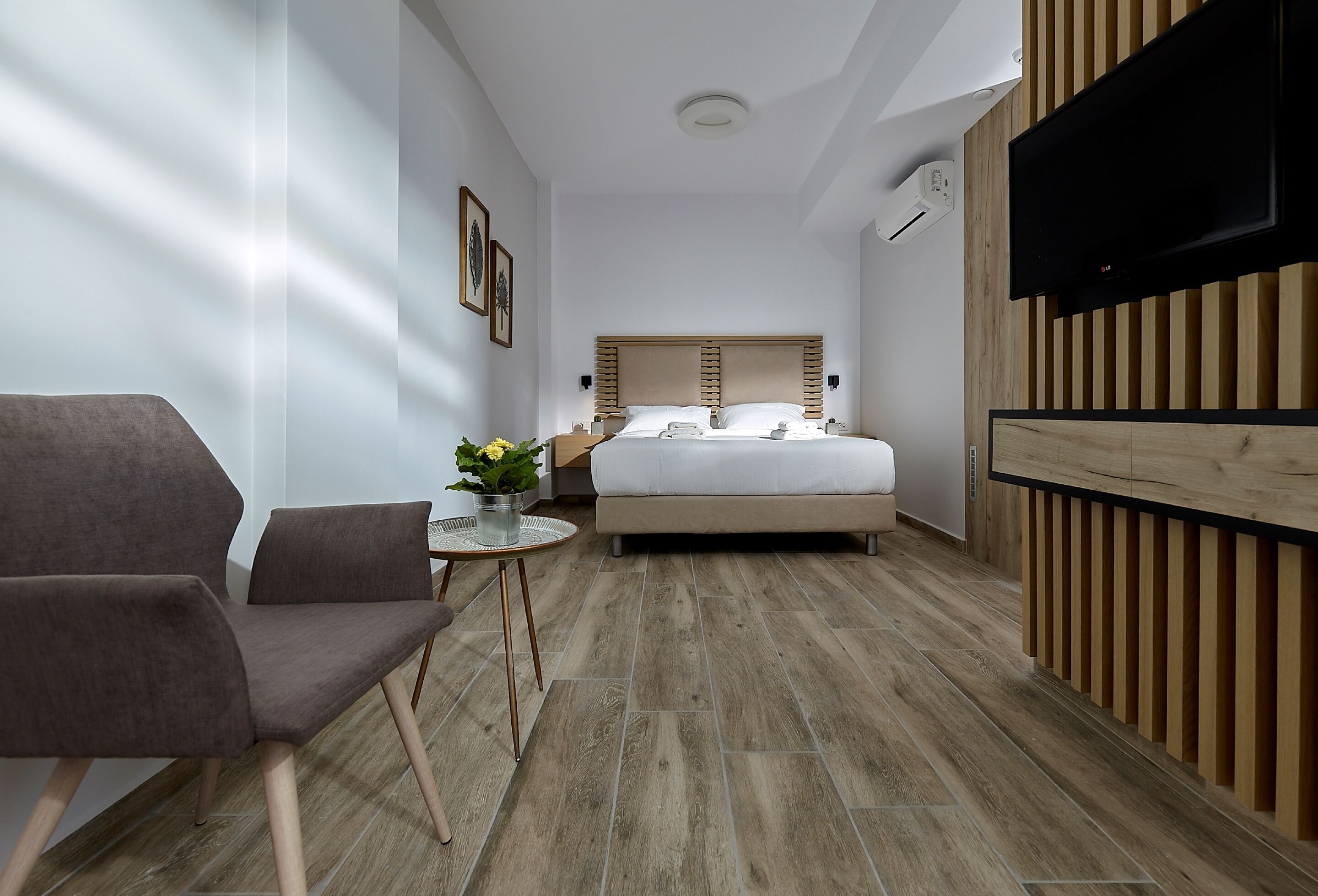 A modern hotel room with a bed, a seating area with a chair and a small table, and a TV mounted on the wall.