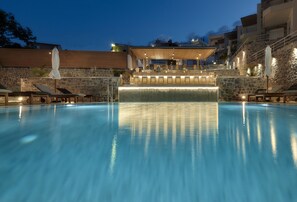 A swimming pool with a waterfall feature, lounge chairs, and a covered seating area. - Seascape Luxury Residences (Malevizi)