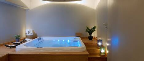 Un spa moderno con una bañera de madera, una planta pequeña y velas.