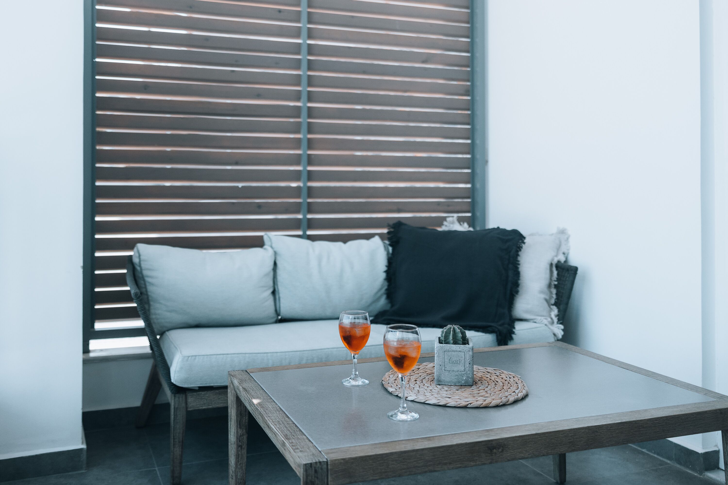 A modern living room with a grey sofa, two glasses of red wine, and a small cactus on a woven coaster.