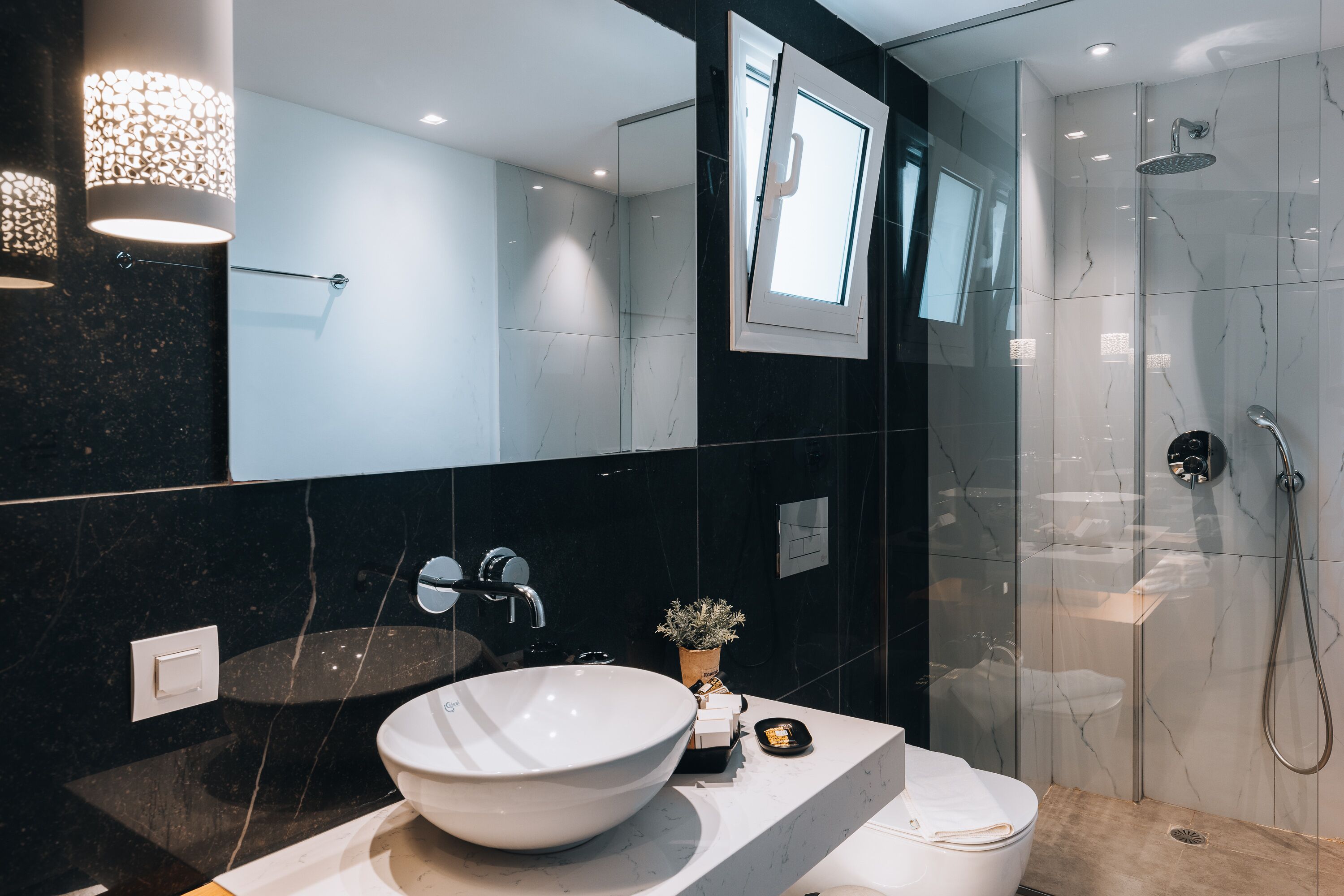 A modern bathroom with a large white sink, a mirror, a shower, and a potted plant.