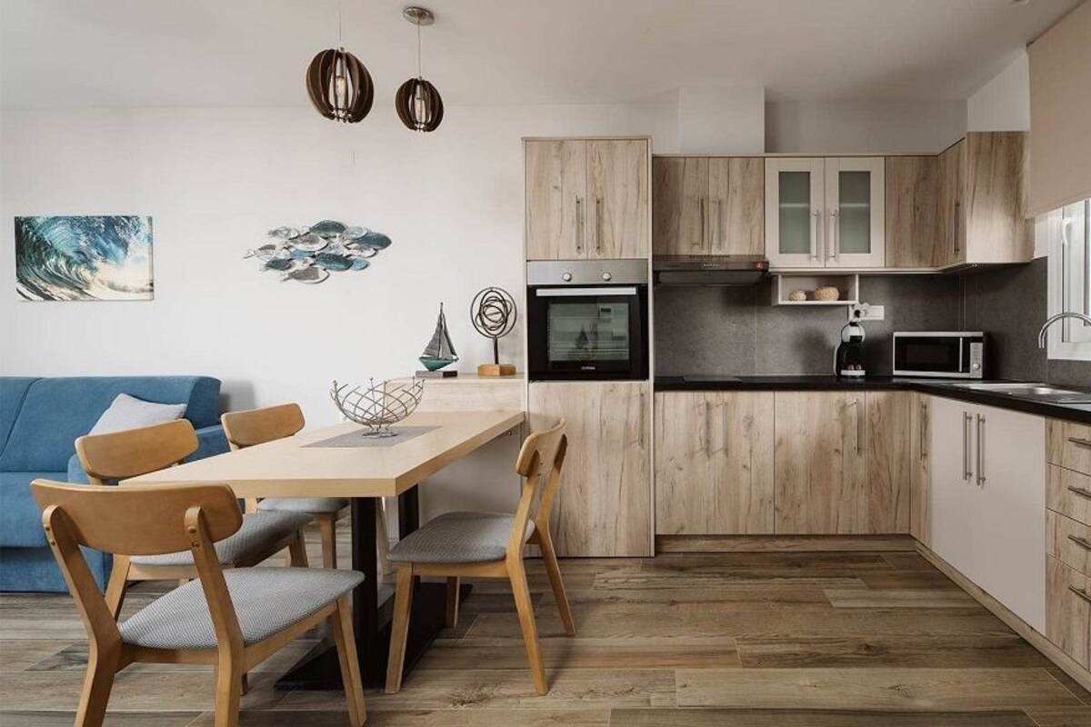 A modern kitchen with wooden cabinets, a dining area with a table and chairs, and a blue sofa.
