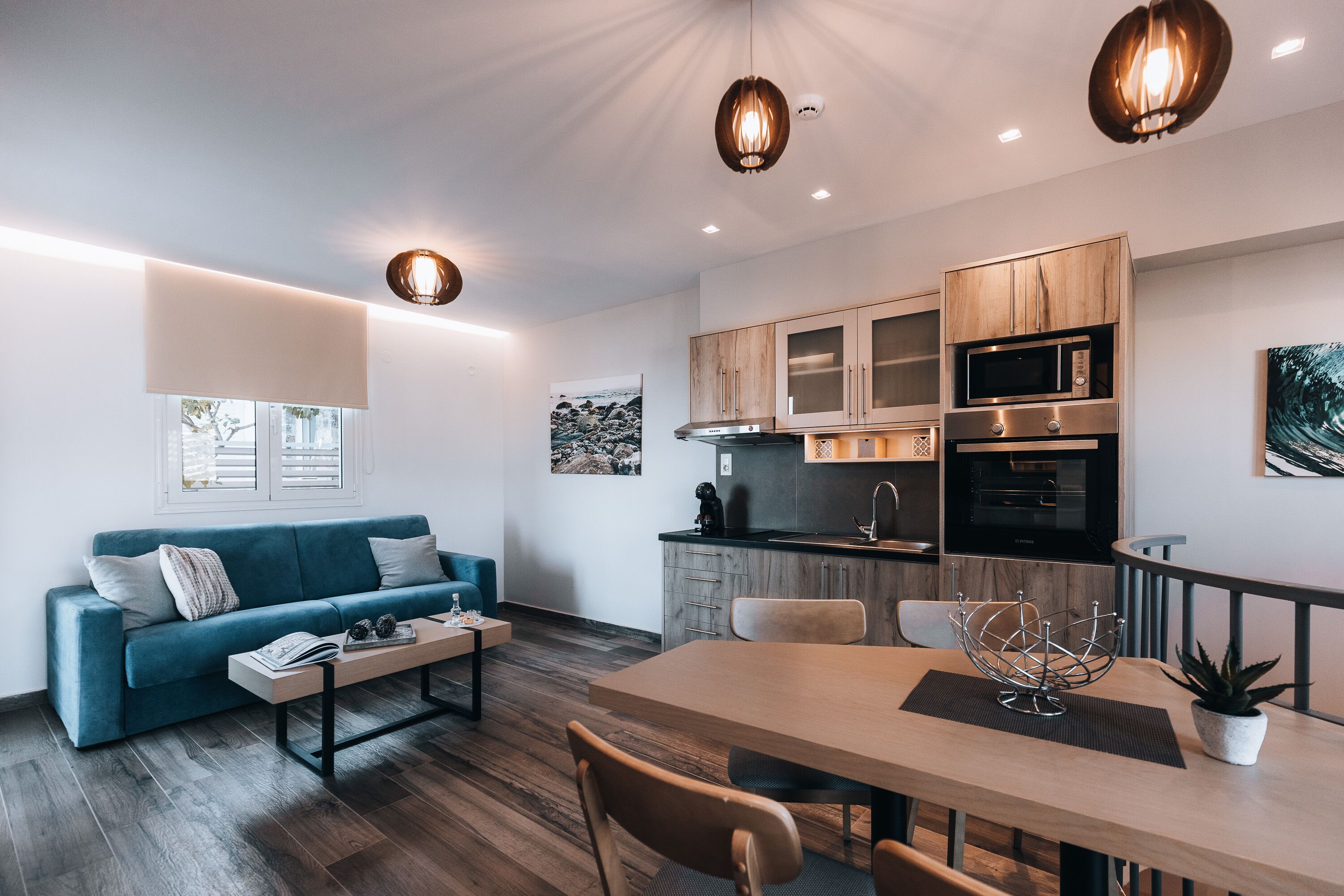 A modern living room with a sofa, coffee table, and dining table. There is a kitchen area with cabinets and appliances.
