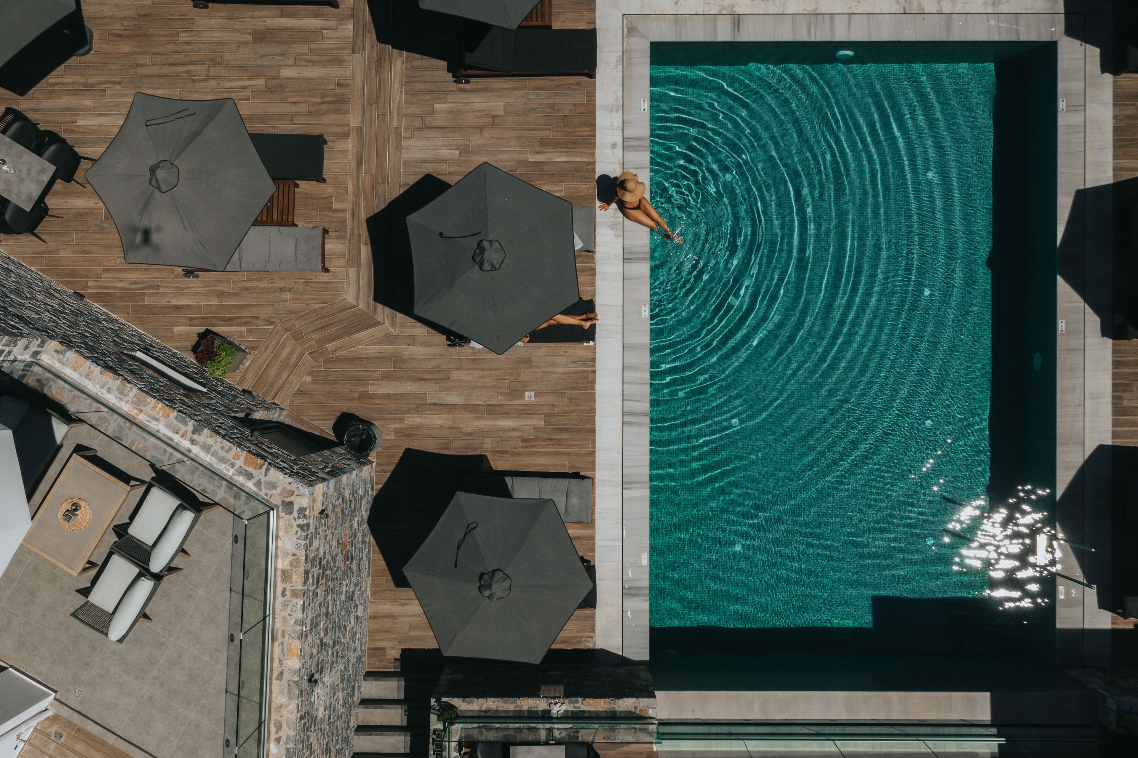 An aerial view of a swimming pool with a person in the water, surrounded by lounge chairs and umbrellas.