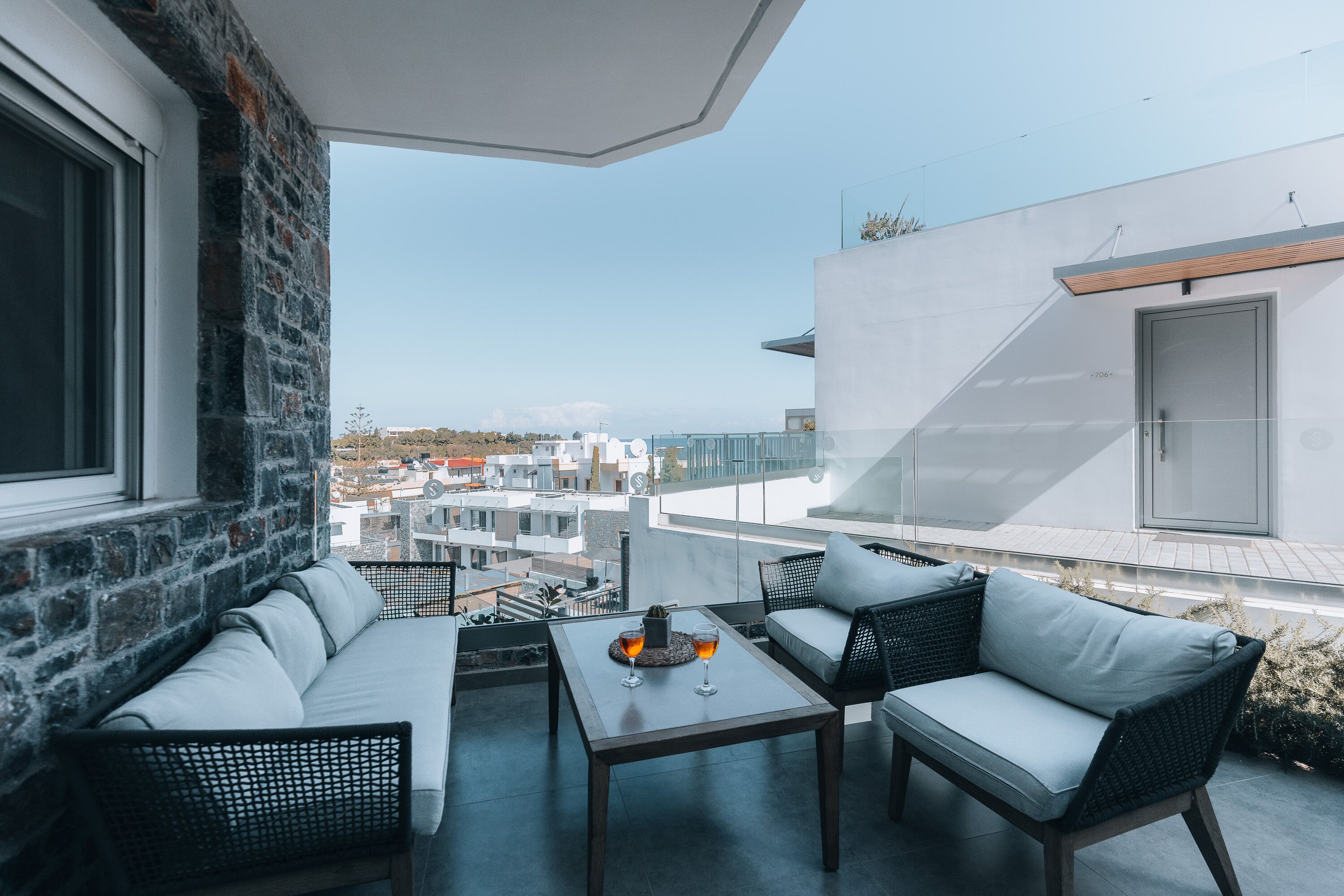 A modern outdoor seating area with a stone wall, a glass railing, and a view of the cityscape.
