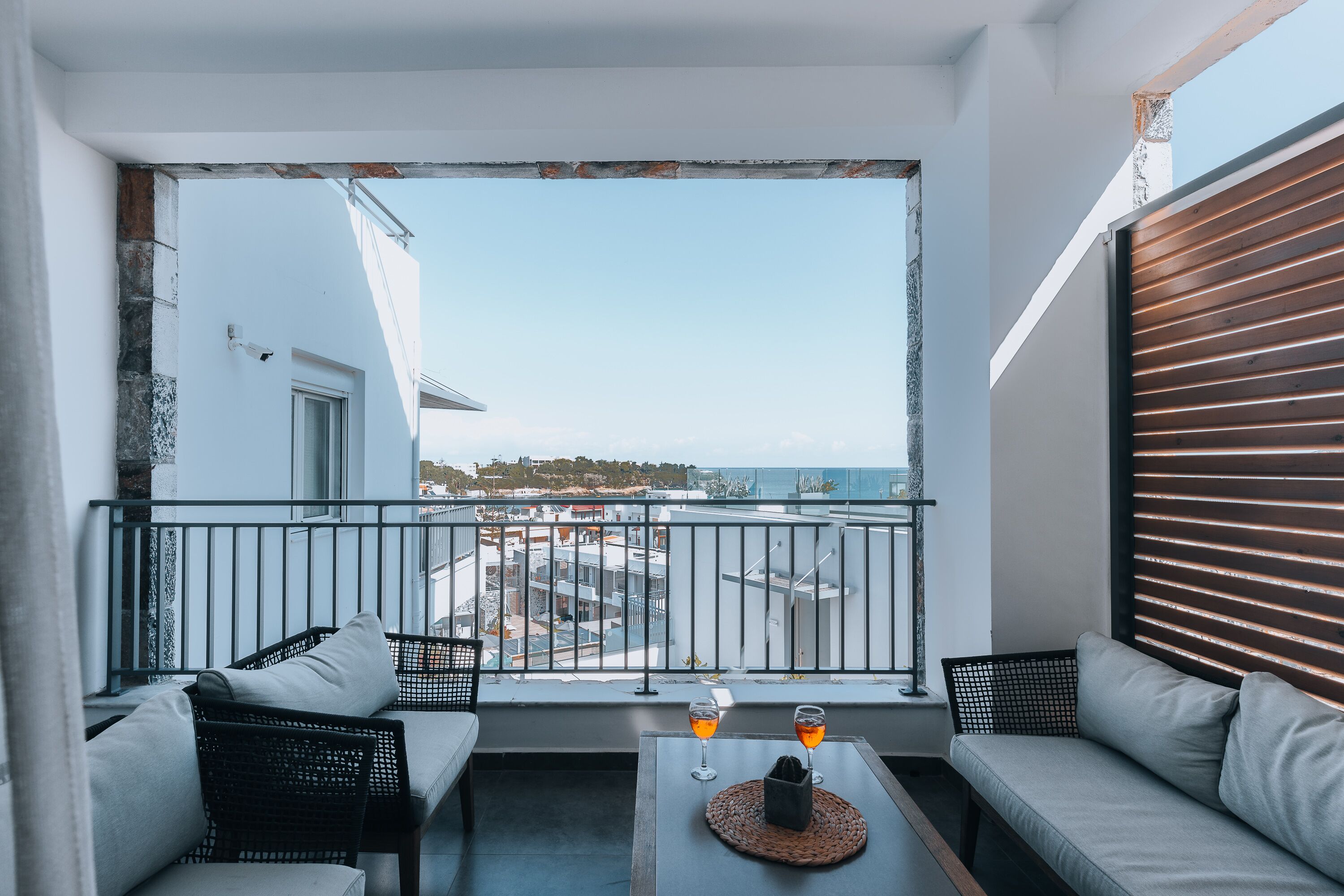 Un balcon avec un canapé, deux fauteuils, une table avec des verres et une vue sur le paysage urbain.
