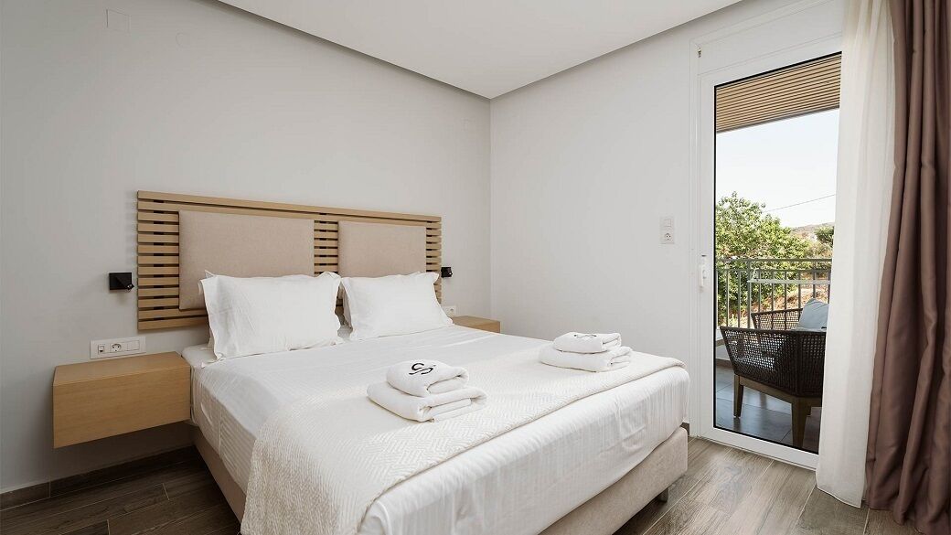 Une chambre d’hôtel avec un lit, une table de chevet, une fenêtre donnant sur un paysage agréable et une porte.