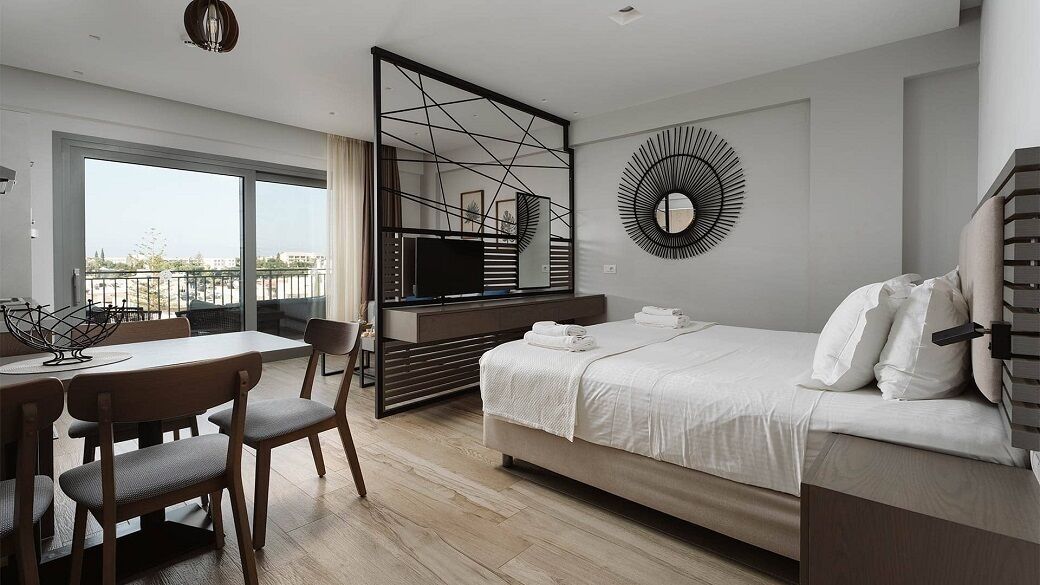 Une chambre d’hôtel moderne équipée d’un lit, d’un bureau avec des chaises, d’une grande fenêtre, d’un téléviseur et d’un élément décoratif mural.