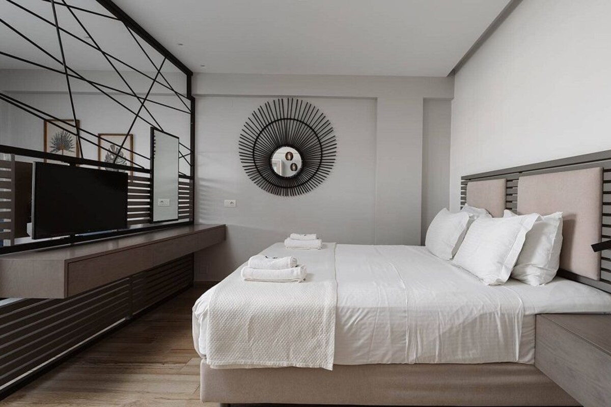 A modern bedroom with a bed, bedside tables, a TV, and a unique wall decoration.