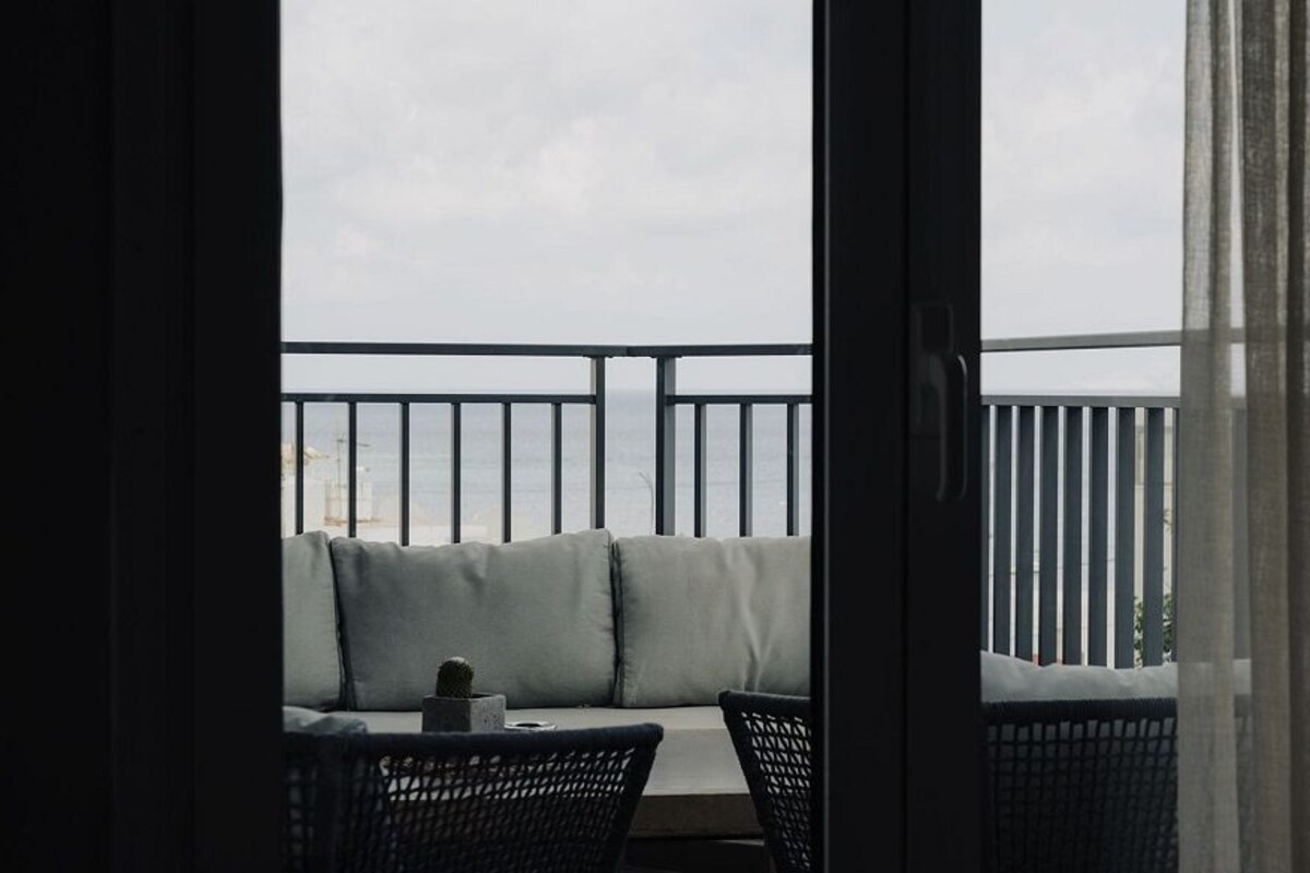 A balcony with a cushioned seating area, a small table with a cup, and a chair.
