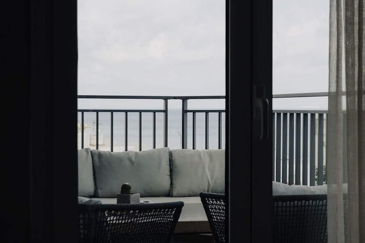 Un balcón con una zona de estar acolchada, una mesita con una taza y una silla.
