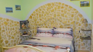 A bedroom with a stone wall, a bed with a pink bedspread, two bedside tables with lamps, and a small shelf with a book and a lamp. - La Casa al Centro (Custonaci)