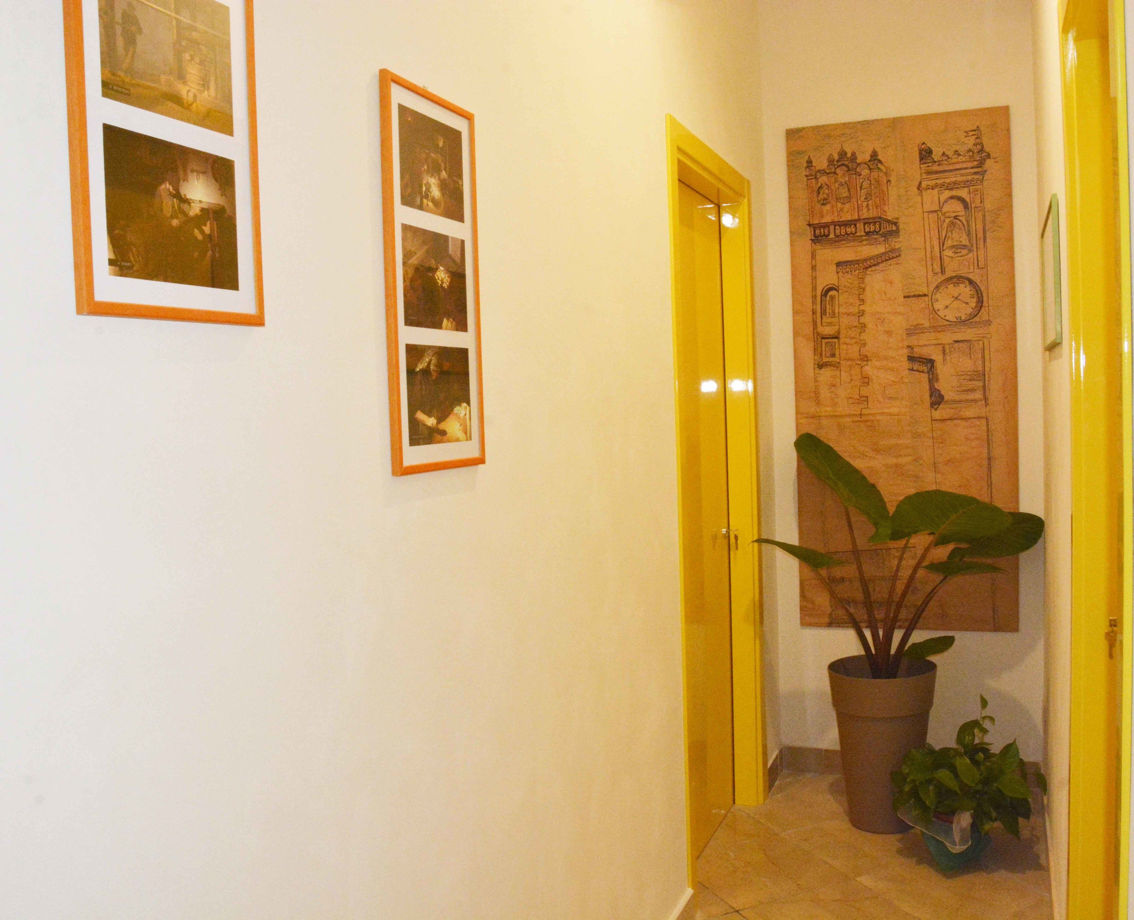 A hallway with a yellow door, a large wall mural, and a potted plant.