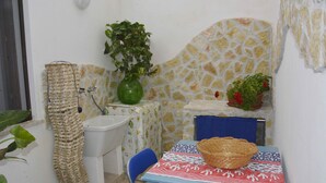 A small bathroom with a sink, a blue chair, a table with a woven basket, and potted plants. - La Casa al Centro (Custonaci)