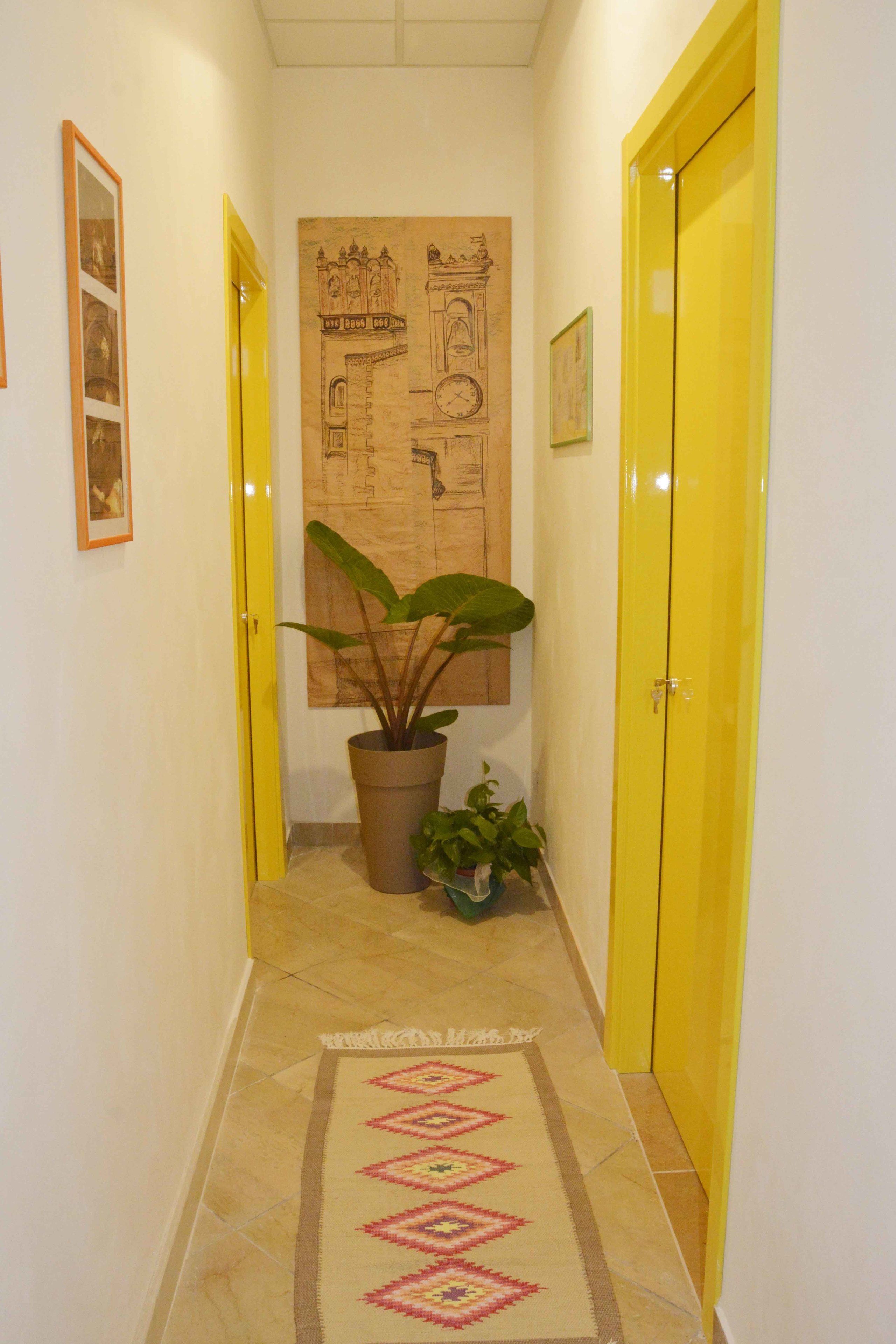 A hallway with yellow doors, a large potted plant, and a patterned rug.