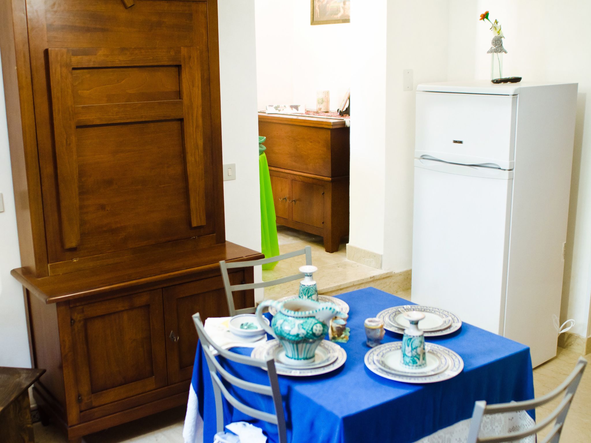 A dining area with a blue tablecloth, wooden cabinets, and a white refrigerator.