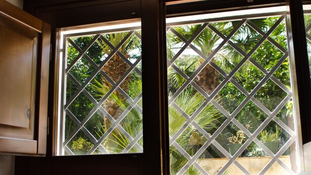 Una ventana con celosía de diseño de diamante, marco de madera y vistas a exuberante vegetación.