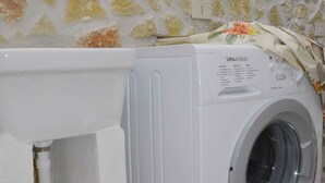 Una lavadora blanca en un baño con pared de piedra y un lavamanos blanco.