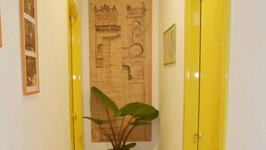 Un pasillo con puertas amarillas, una planta grande en maceta y un tapete estampado.