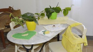 Una mesa con una planta amarilla, un corazón de ganchillo verde, un mantel blanco con diseño de limón y un bolso amarillo.