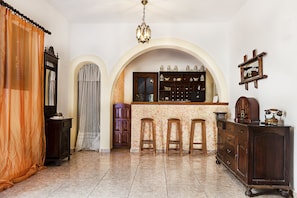 A room with a bar area, wooden furniture, and a chandelier.