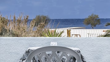 Una zona de estar exterior blanca con vista al mar y una terraza de madera al fondo.