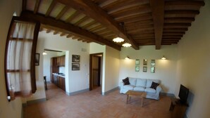 A spacious living area with a wooden ceiling, a sofa, a coffee table, and a television on a wooden stand. - Agriturismo Il Beccafico Alpaca (Gubbio)