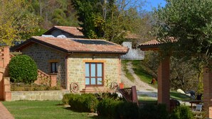 A stone house with a tiled roof, a window with curtains, and a small garden with a bench. - Agriturismo Il Beccafico Alpaca (Gubbio)