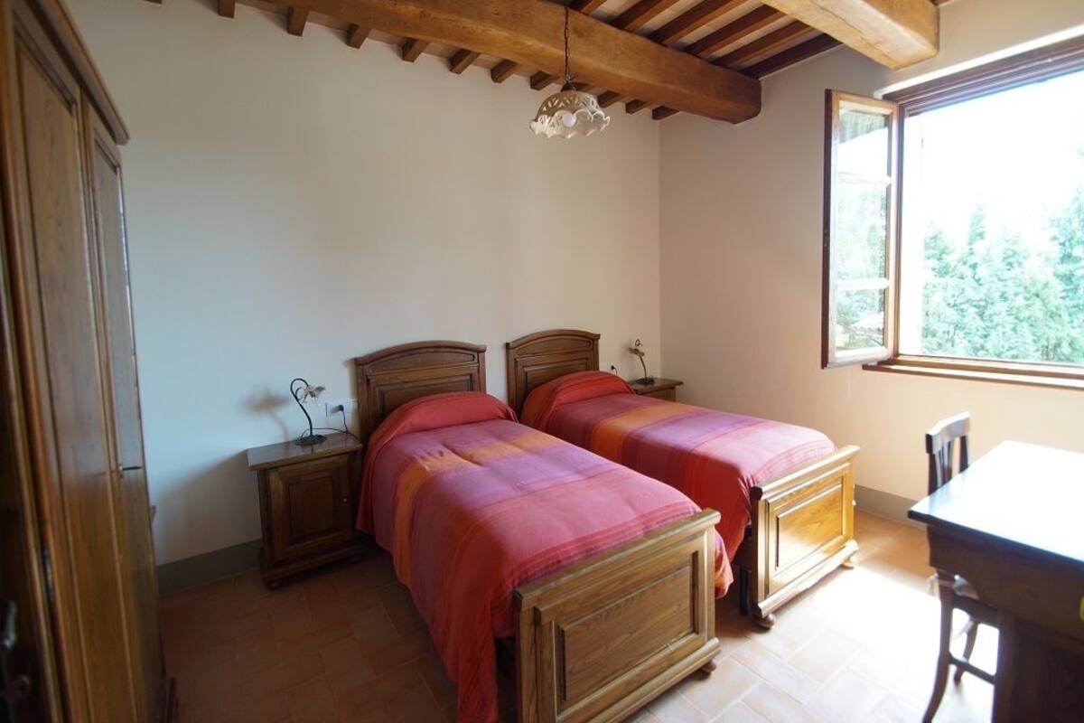 Une chambre à coucher avec deux lits en bois, une table de chevet, un bureau et une fenêtre donnant sur des arbres.