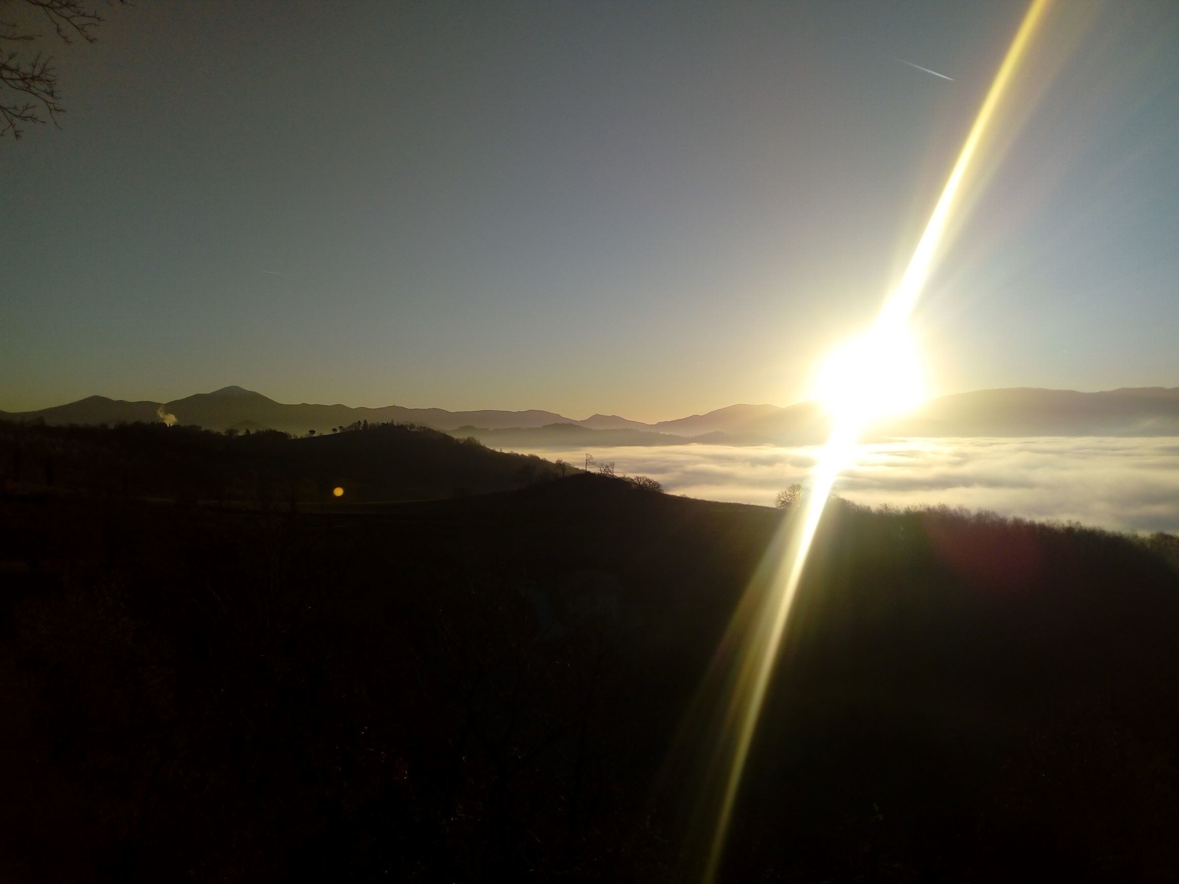 Un paisaje con el sol poniéndose o saliendo detrás de una cadena montañosa, iluminando la escena.
