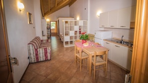Eine gemütliche Küche mit Holzbalken, einem Esstisch mit Stühlen, einer Couch und einem weißen Schrank.
