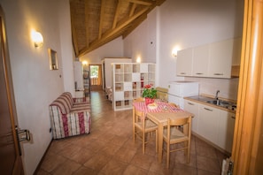 A cozy kitchen with wooden beams, a dining table with chairs, a sofa, and a white cabinet. - Val Rendena Village (Porte di Rendena)
