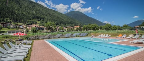 Une piscine entourée de chaises longues et de parasols, le tout niché au cœur d’un paysage montagneux.